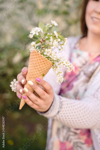 Beautiful waffle cone with ice cream decorated with flowers in the girl’s hand with multi-colored bright manicure © Anna-Tsygankova