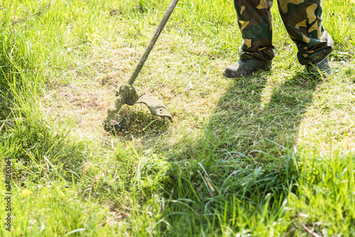 Worker mows grass on the site with a gasoline mower. A man takes care of the lawn with a string trimmer.
