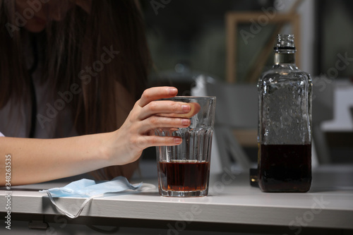 Drinking problem alcoholism during coronavirus isolation quarantine time concept. Hand holding glass with alcohol drink. face mask on background.