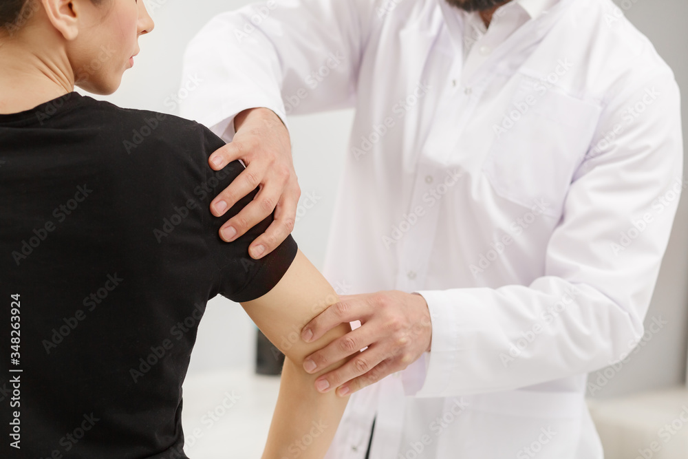 Obraz premium Male doctor examining female patient suffering from elbow pain. Medical exam. Chiropractic, osteopathy, post traumatic rehabilitation,sport physical therapy. Alternative medicine, pain relief concept.