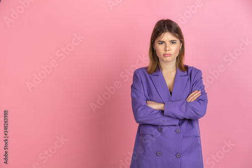Sad, hands crossed. Caucasian young woman's portrait isolated on pink studio background. Beautiful female model in purple jacket. Concept of human emotions, facial expression, sales, ad. Copyspace.