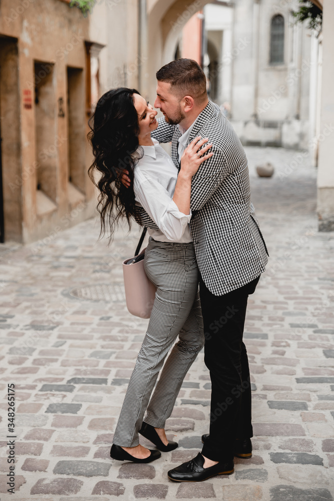 Charming girl with long brown hair and a man with a beard kissing on the background of the morning city. Newlyweds on their wedding day