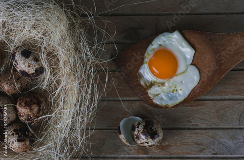 Nido de paja y heno con huevos de codorniz, huevo frito sobre cuchara de madera y cascara de huevos  sobre palet de madera