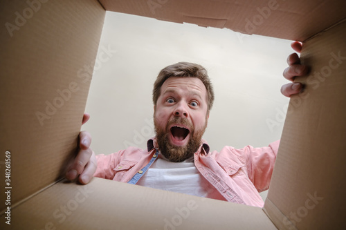 Joyful, surprised Caucasian man unpacks a delivered box with a parcel or a gift. Unboxing inside view. photo
