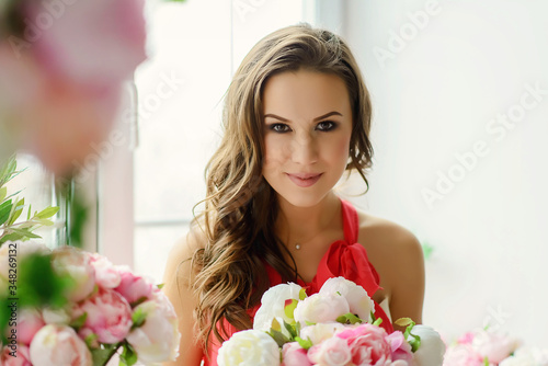 Foto Beautiful young brown-eyed woman with a bouquet of peonies flowers in her hands near the window