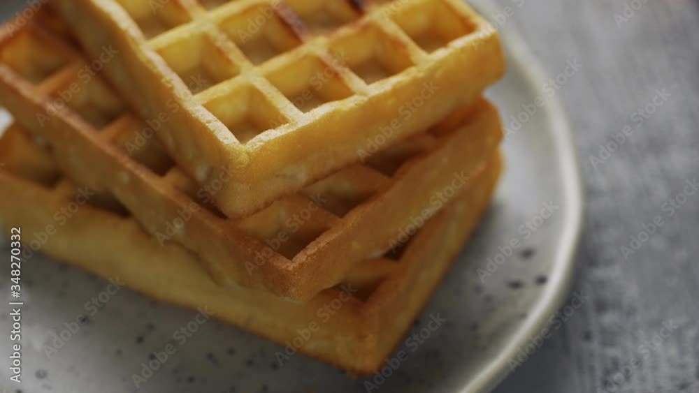 Waffles with powdered sugar.. Sprinkling powdered sugar on the three waffles on the plate. Waffles with powdered sugar.. Sprinkling powdered sugar on the three waffles on the plate.