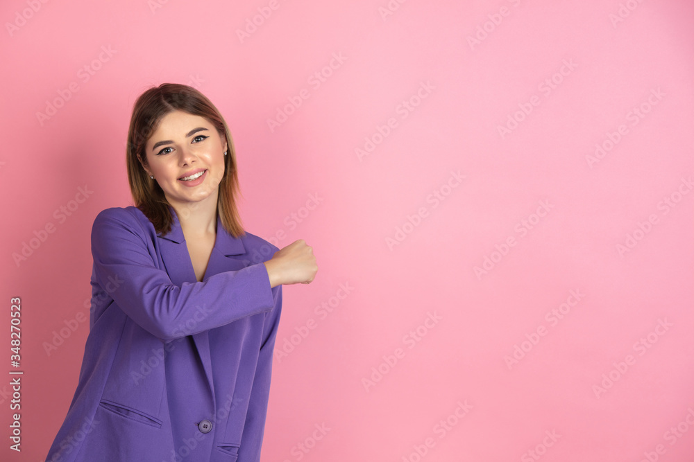 Pointing, smiling. Caucasian young woman's portrait isolated on pink studio background. Beautiful female model in purple jacket. Concept of human emotions, facial expression, sales, ad. Copyspace. Pointing, smiling. Caucasian young woman's portrait isolated on pink studio background. Beautiful female model in purple jacket. Concept of human emotions, facial expression, sales, ad. Copyspace.
