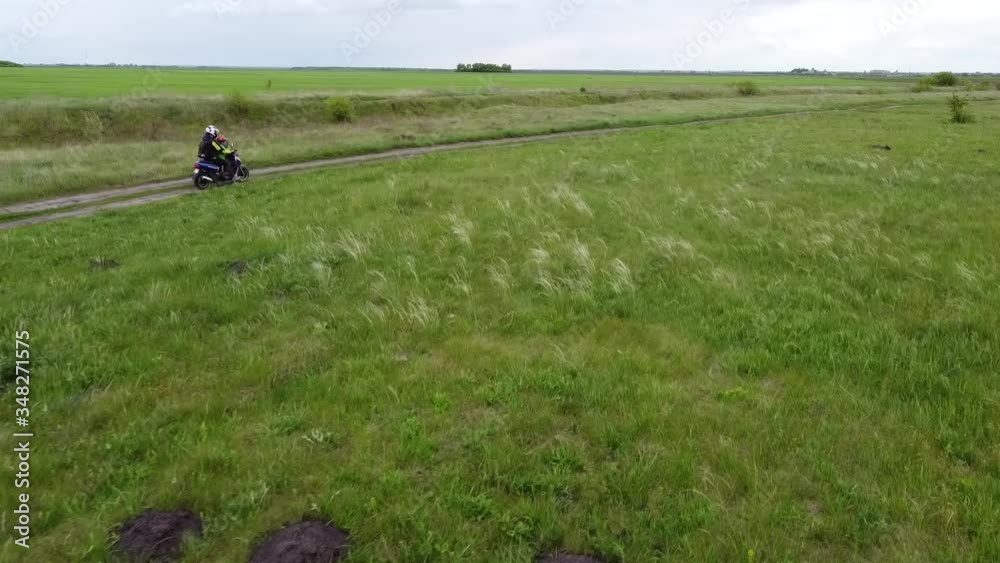 A girl and a child riding a moto scooter or motorcycle along a dirt road between fields.Aerial, drone footage.7