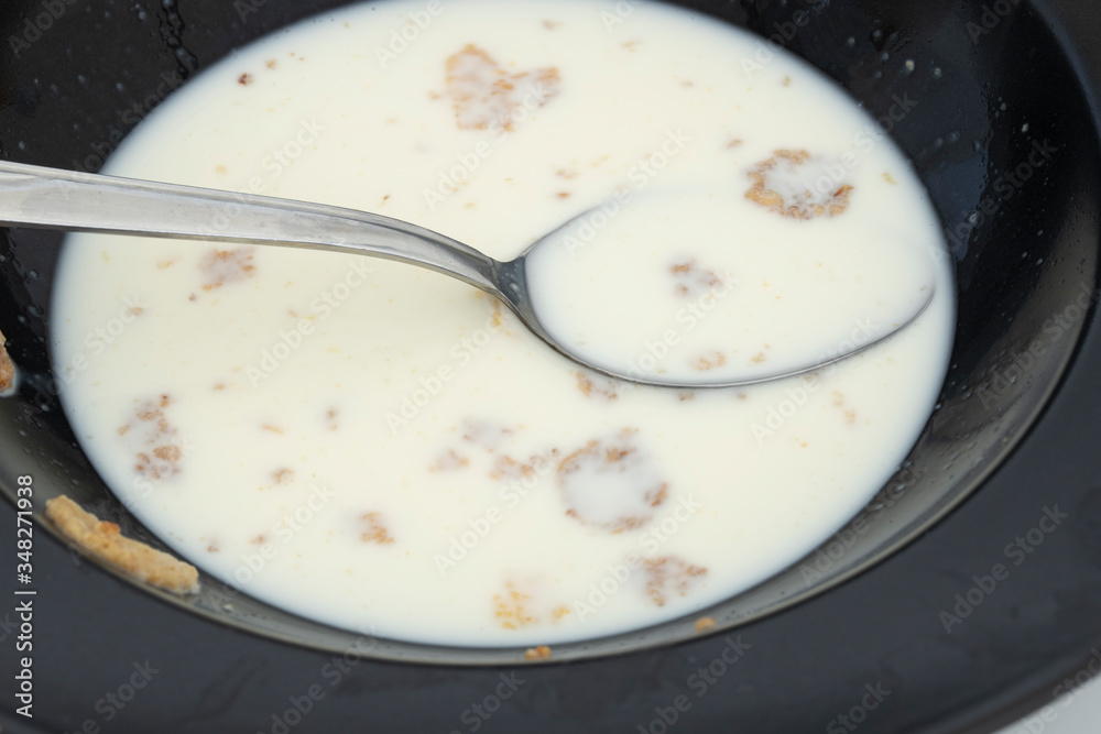 Some milk and cornflakes in a black plate. Low and hungry Close up. Some milk and cornflakes in a black plate. Low and hungry Close up.