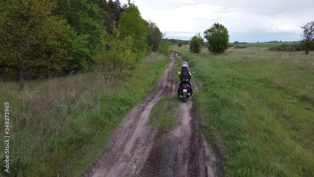A girl riding a moto scooter or motorcycle along a dirt road between field and forest. Aerial, drone footage. A girl riding a moto scooter or motorcycle along a dirt road between field and forest. Aerial, drone footage.