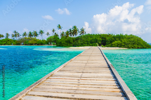 Wooden bridge over turquoise water to a tropical island in the Maldives 