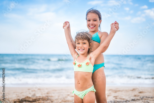 Two cute positive little girls sisters raised their hands up while swimming at sea during the holidays on a warm summer day. Concept of healthy and joyful children
