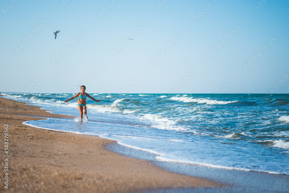 Joyful little girl enjoys a beach day while relaxing at sea on a sunny warm summer day. Summer vacation and relaxation concept Joyful little girl enjoys a beach day while relaxing at sea on a sunny warm summer day. Summer vacation and relaxation concept