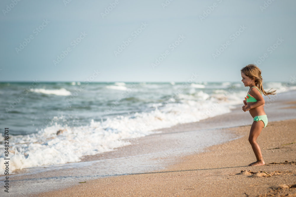 Joyful little girl enjoys a beach day while relaxing at sea on a sunny warm summer day. Summer vacation and relaxation concept