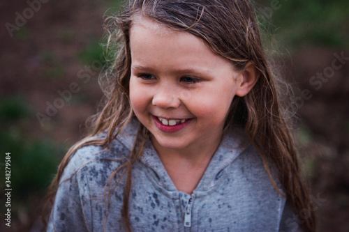 Cute girl portrait outdoors, happy kid wet hair walking under the rain