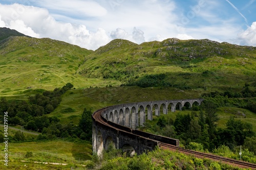 The landscape with famous Glenfinnan Viaduct in Scotland with a historic steam train in the background with cloud shadows