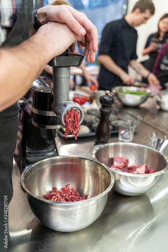 Man pushing a piece of raw meat into an electric grinder