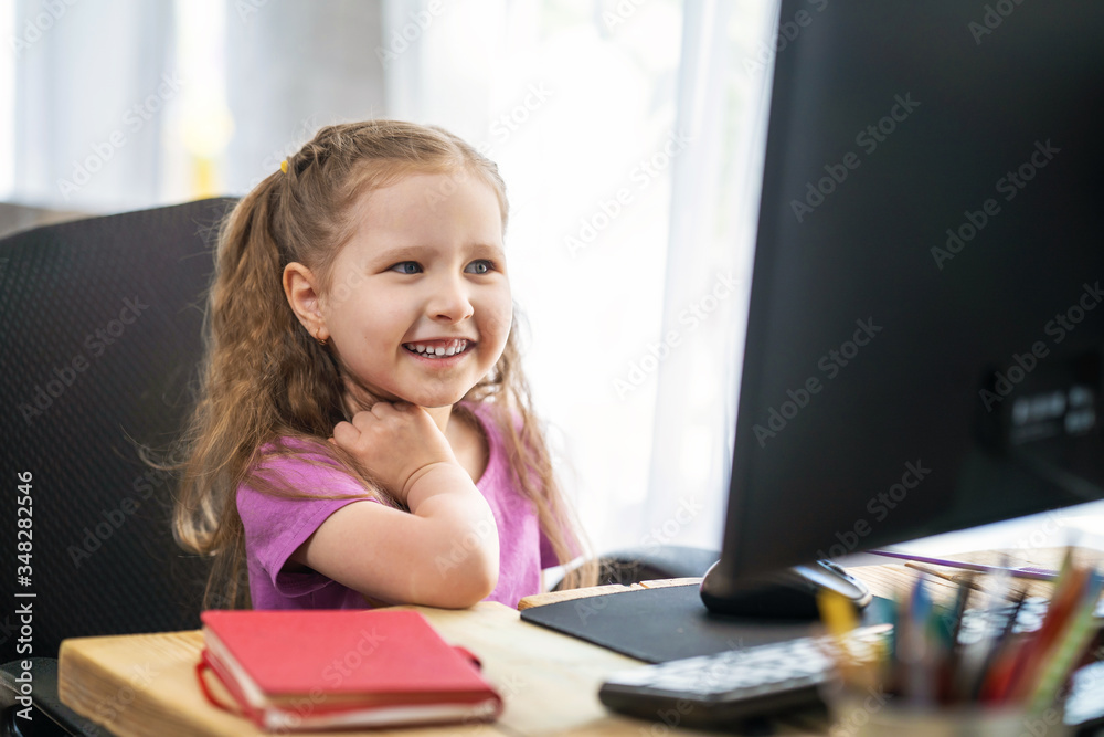 Fototapeta premium A little cute girl using a computer for remote e-learning.