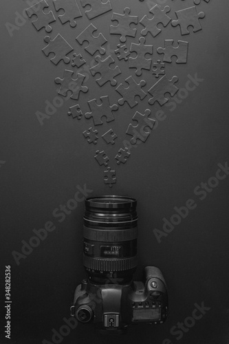 professional camera lies on a black background next to black puzzles that accumulate to the camera lens photo