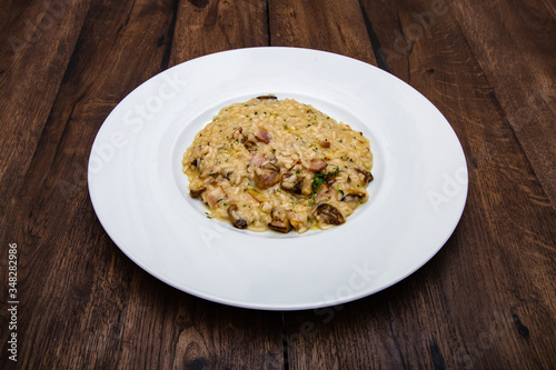 Italian risotto with porcini mushrooms and bacon in a white plate on a wooden table.