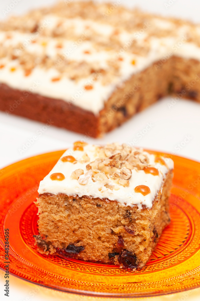 Slice of cake with white cream, caramel spots and nuts on white background