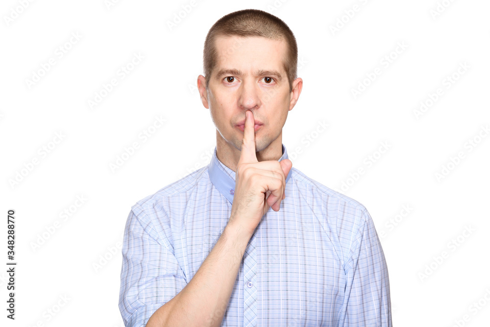 Serious man in a classic blue shirt; shows a gesture of silence, the preservation of silence and mystery; put his index finger to his lips; look into the camera. Isolated Serious man in a classic blue shirt; shows a gesture of silence, the preservation of silence and mystery; put his index finger to his lips; look into the camera. Isolated