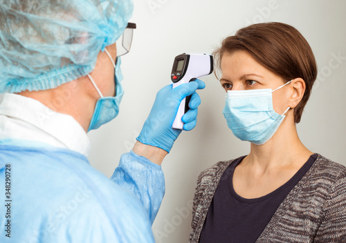 The doctor checks the temperature on the forehead with an infrared thermometer for the presence of a virus.