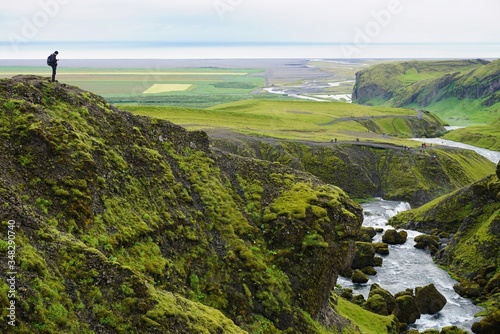 the Skogar river flows towards the ocean, tourists walk along the river, a man stands on a high green hill, the nature of Iceland photo