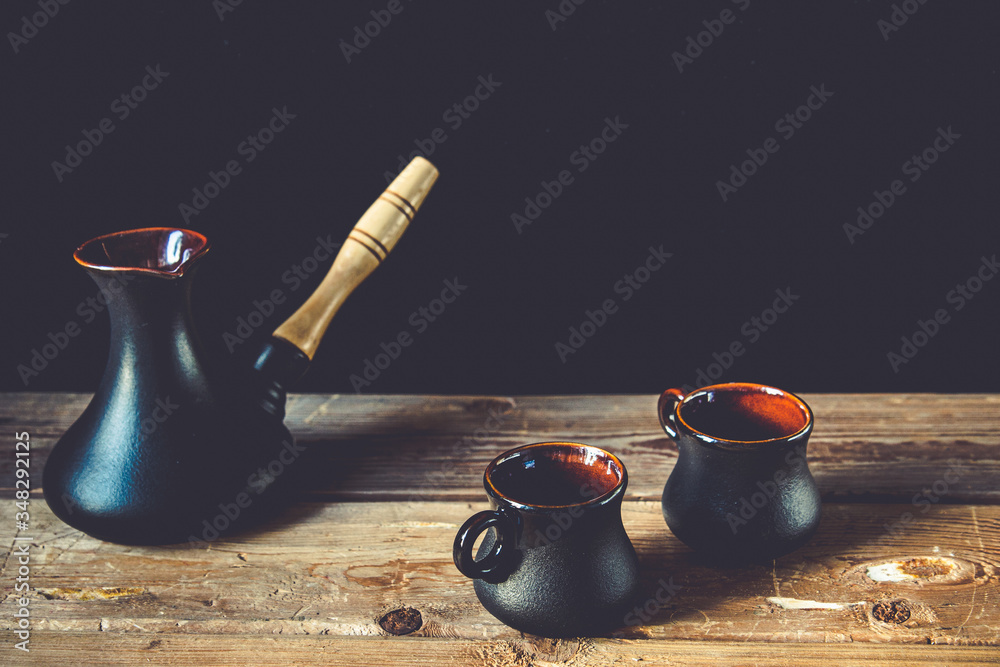 Two black cups for coffee and black turk on the old wooden table and black background with retro filtr. Cozy home idea. Sweet home - obrazy, fototapety, plakaty 