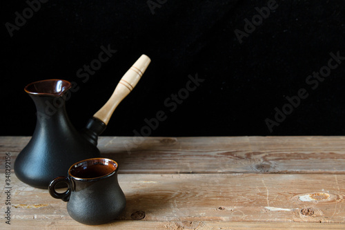 One black cup for coffee and black turk on the old wooden table and black background, place for text. Sweet home