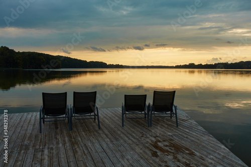 An empty pier with deckchairs on a calm lake, at sunset