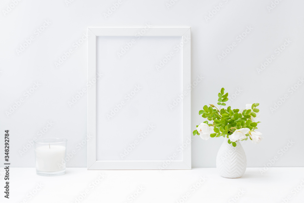 Home interior with decor elements. Mockup with a white frame and small flowers and green leaves in a vase on a light background Home interior with decor elements. Mockup with a white frame and small flowers and green leaves in a vase on a light background