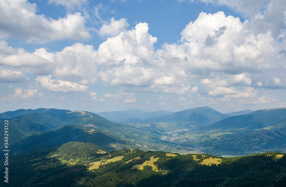 Beautiful landscape from a height. Typical Carpathian village in a valley, forest and mountains under blue sky with white clouds. Carpathians, Ukraine