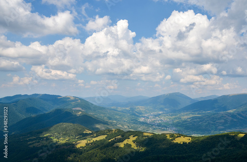 Beautiful landscape from a height. Typical Carpathian village in a valley, forest and mountains under blue sky with white clouds. Carpathians, Ukraine © Dmytro