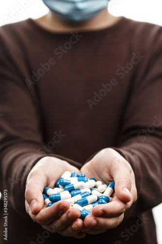 Child in medical mask holds handful of pills.