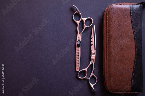 a pair of scissors for a hairdresser, a leather bag for them lie on a textured background