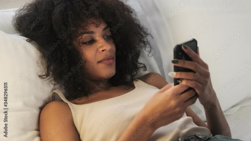 Young pretty african curly woman indoors at home using mobile phone Young pretty african curly woman indoors at home using mobile phone