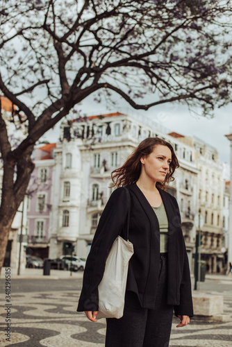 Half length portrait of attractive young confident woman looking aside. Serious caucasian girl with canvas shopping bag standing at Rossio square in Lisbon, Portugal © Olga