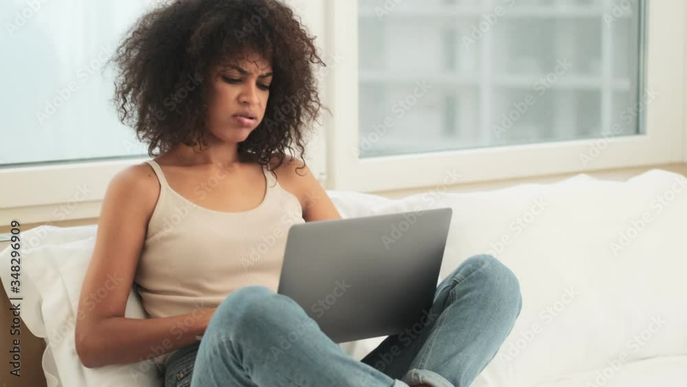 Serious tired african curly woman indoors at home using laptop computer Serious tired african curly woman indoors at home using laptop computer