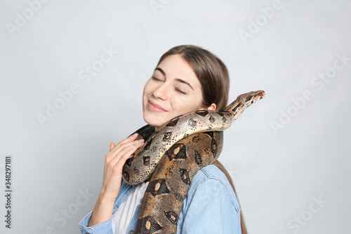 Young woman with boa constrictor on light background. Exotic pet