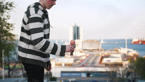 Young teenage boy playing kendama outside in city on sea port background