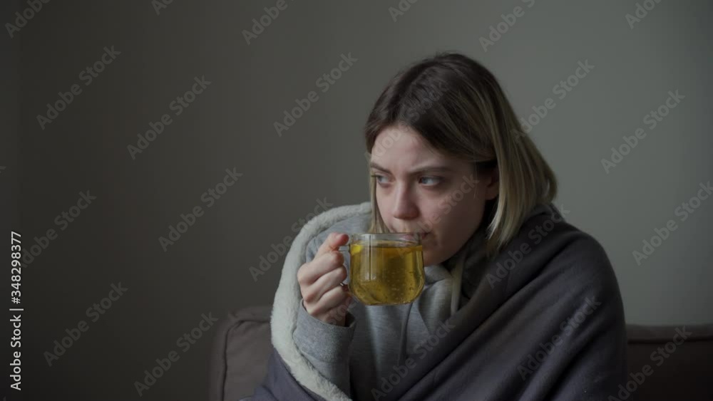 Beautiful young blonde girl drinks hot tea in a transparent mug. Sign of coronovirus, flu, acute respiratory disease. Beautiful young blonde girl drinks hot tea in a transparent mug. Sign of coronovirus, flu, acute respiratory disease.