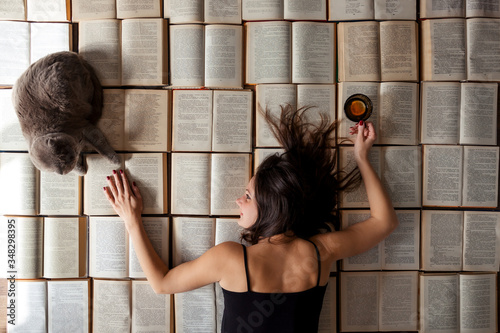 Tired teacher woman lying at books  background with cup of tee after hard work day and relaxing with cat