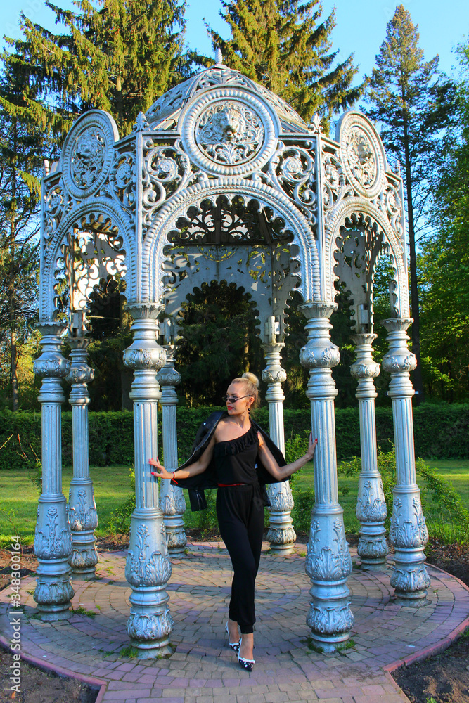 A silver metal gazebo and a model standing nearby and a posing woman. Photoshoot in the park, vertical photo.