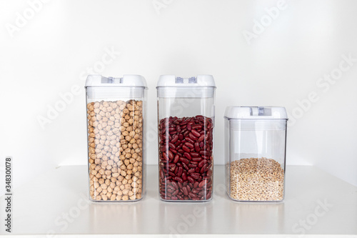Set of Three Clear Pantry Containers In a Row Filled with Non-Perishable Foods-- Dried Beans and Grains