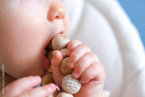 eco wood toys. baby game. Little clever caucasian child playing natural toys on highchair. games for early development. Toy in kids mouth close up photo
