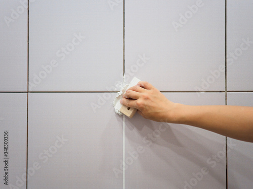 Grouting between tiles in the bathroom. Female hand holds a spatula. Repairs photo
