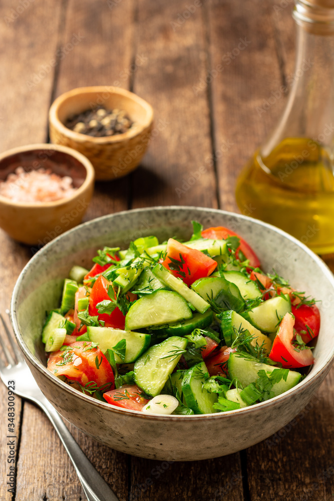 Fresh vegetable salad with cucumber, tomato and greens in bowl on rustic wooden table