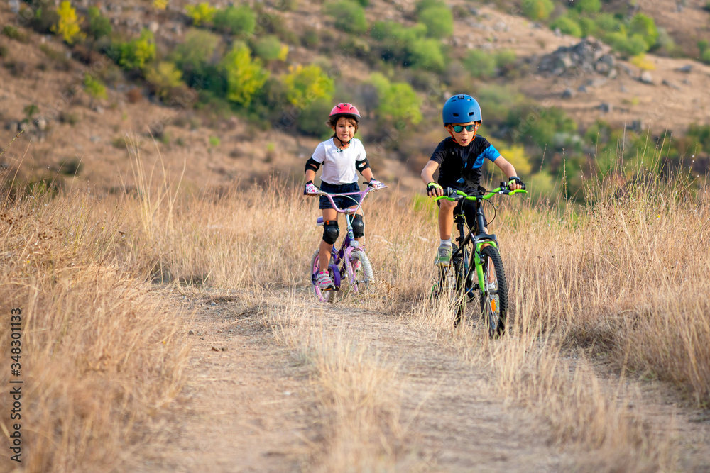 Happy girl and boy having fun in autumn park with a bicycle on beautiful fall day. Active kids wearing bike helmet