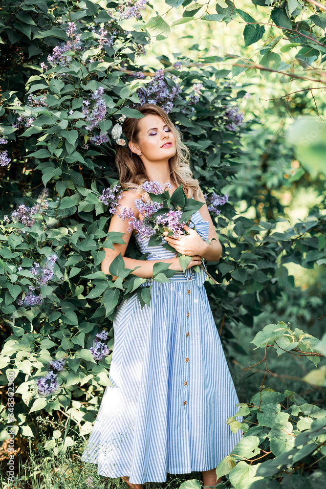 A beautiful happy young woman enjoys the smell in a blooming spring Lilac garden. Happy beautiful woman enjoying nature. A trendy modern look .